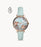 The light teal leather strap attaches to the subtle rose gold tone bezel. The slim rose gold hour markers and hands are easily visible against the opalescent dial. The light blue dial is adorned with a flowery pattern.
