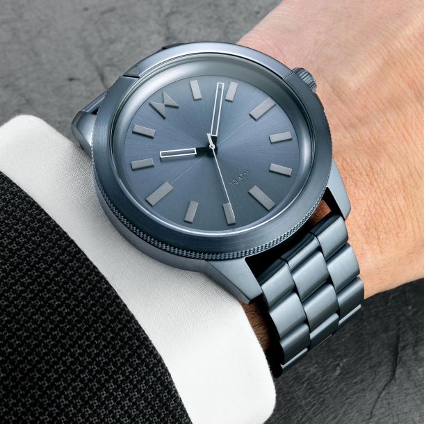 Men's Minimal Sport Baltic Blue, Blue Gunmetal dia, white markers, white hour and minute hands and black second hand. Rotating divers bezel, MVMT logo placed at 12 o'clock marker, 10 ATM Water Resistance indicator at 6 o'clock marker.